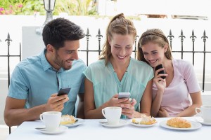 Portrait of three happy friends reading text message in the caf